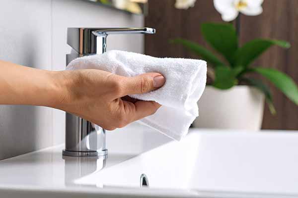 Hand säubert Armatur mit einem weissen Tuch
